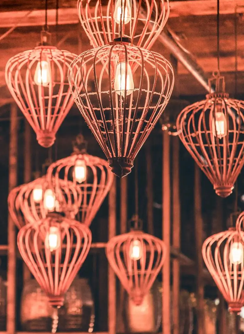 A cluster of vintage-style pendant lights with intricate wire frames, glowing warmly against a rustic backdrop.